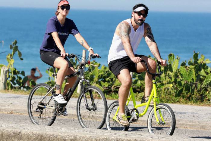 Juliano Cazarré anda de bike com a mulher na orla da praia